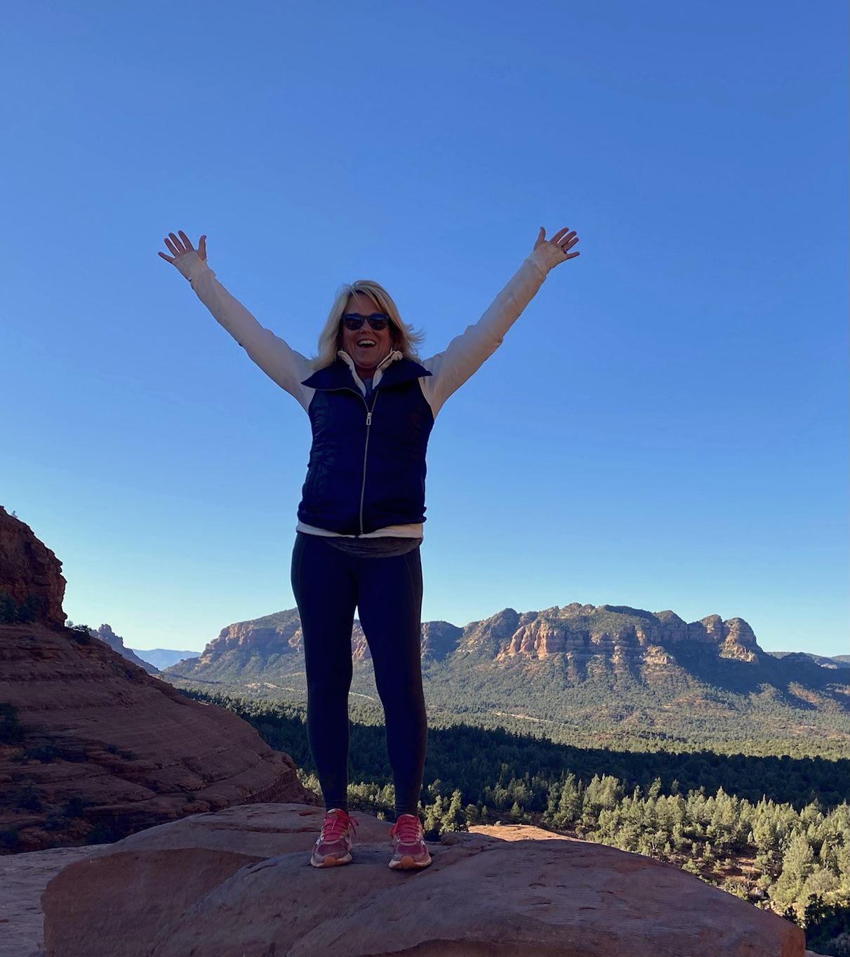 A woman on a mountain overlook, arms raised to a wide morning sky