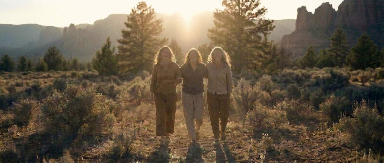 Three women walking arm in arm toward you out of a golden dawn