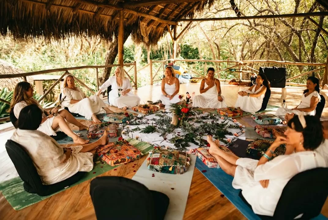 A circle of women together under the palapa, flowers at its heart