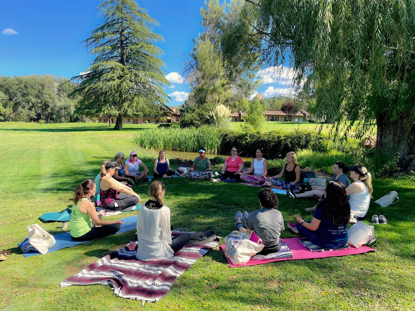 A circle of women gathered on the grass under tall pines
